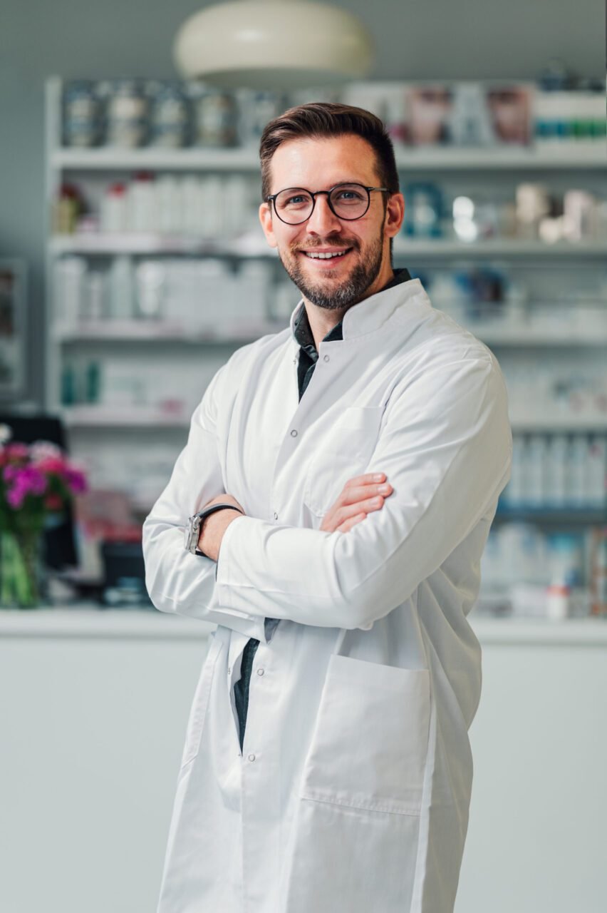 A pharmacy expert is standing in the drug store and smiling at the camera 